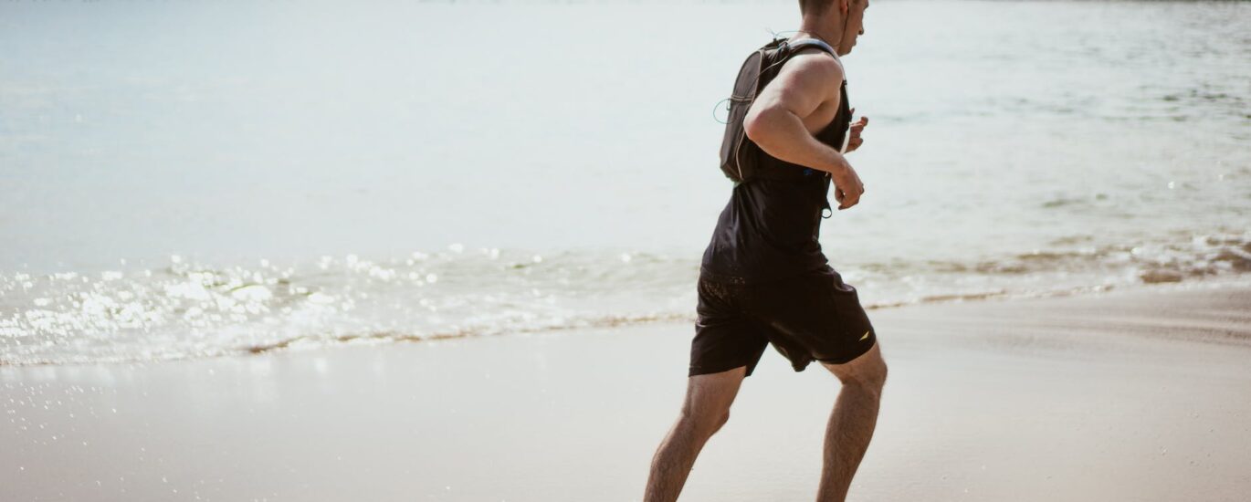 man wearing black tank top and running on seashore
